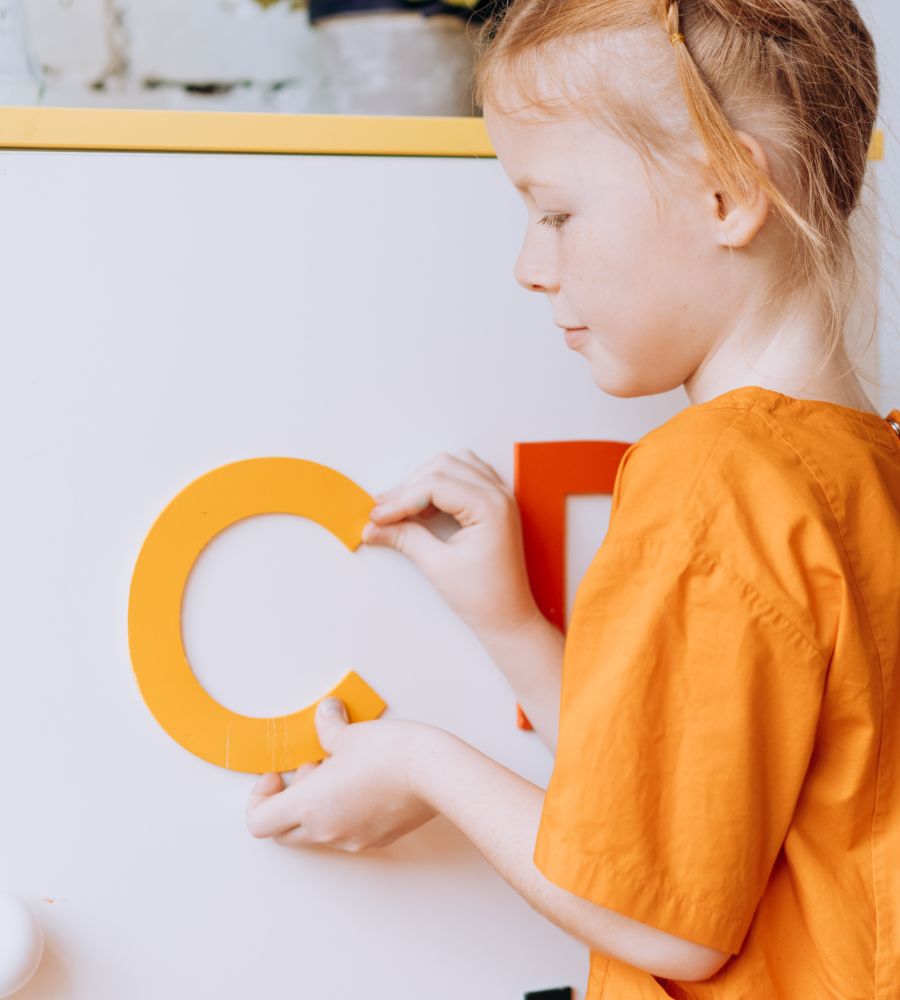 A young learner placing alphabet letters on a whiteboard